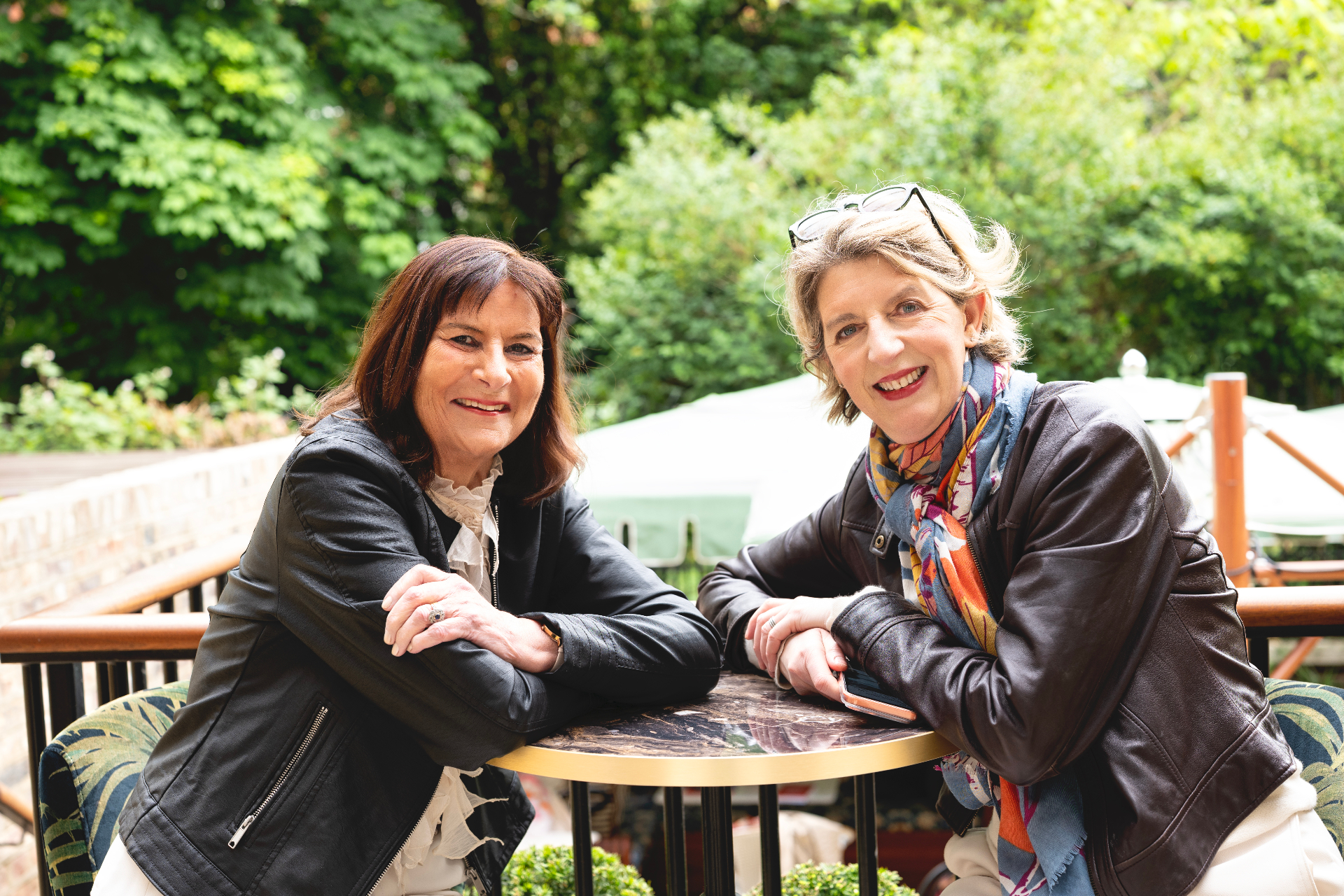 Louise Ballard and Victoria Tomlinson in leather jackets seated at a table outdoors